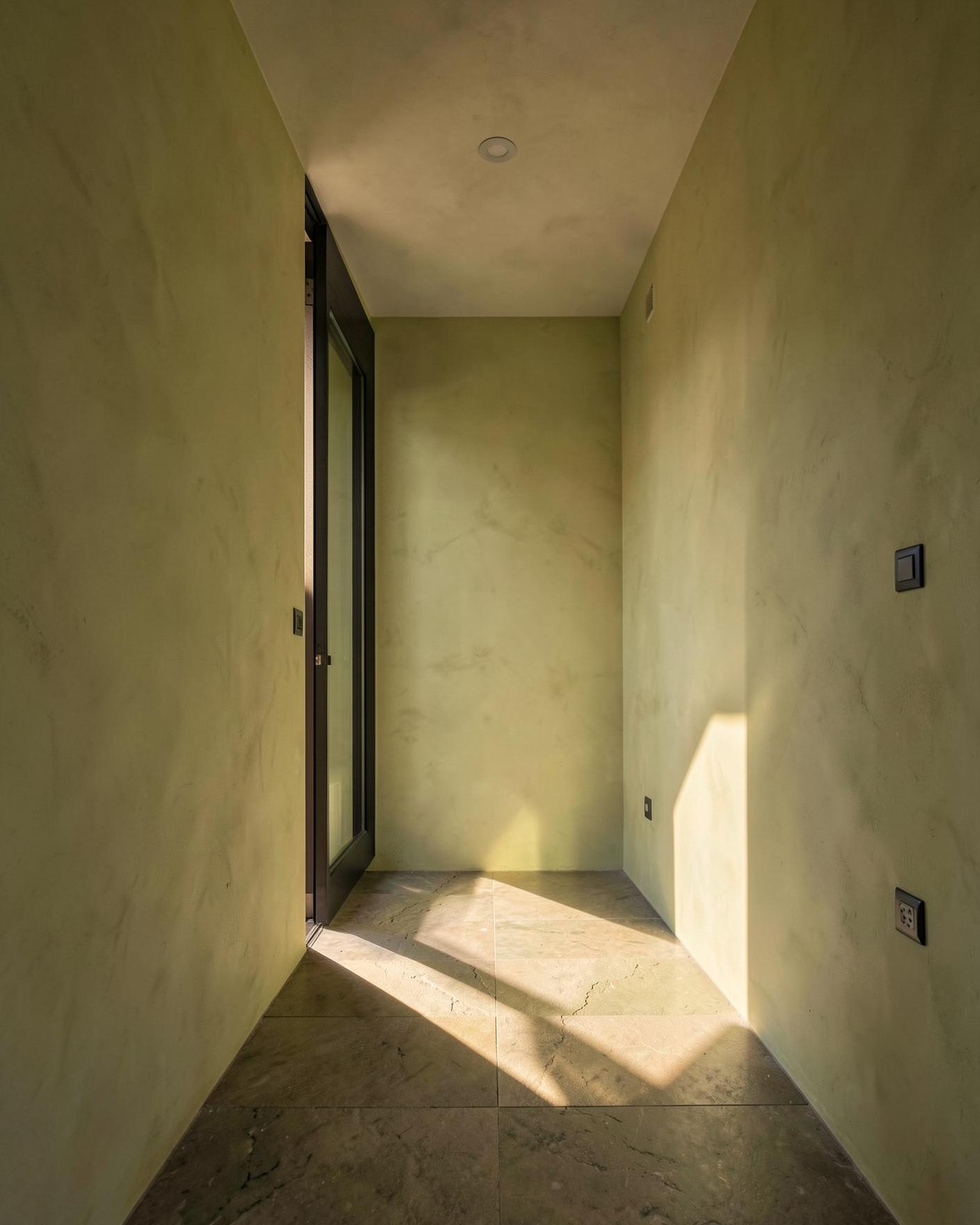 A narrow lime-plaster passage crossed by geometric warm daylight