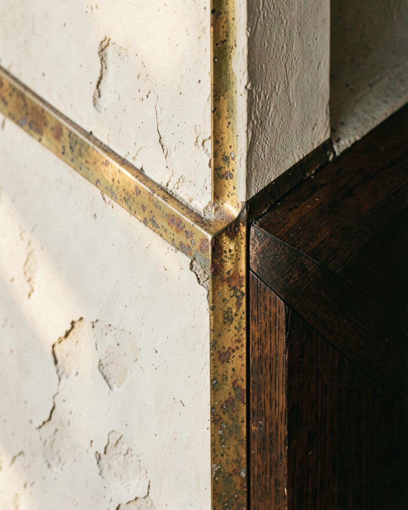 Weathered lime plaster, brass and dark timber meeting at a precise junction